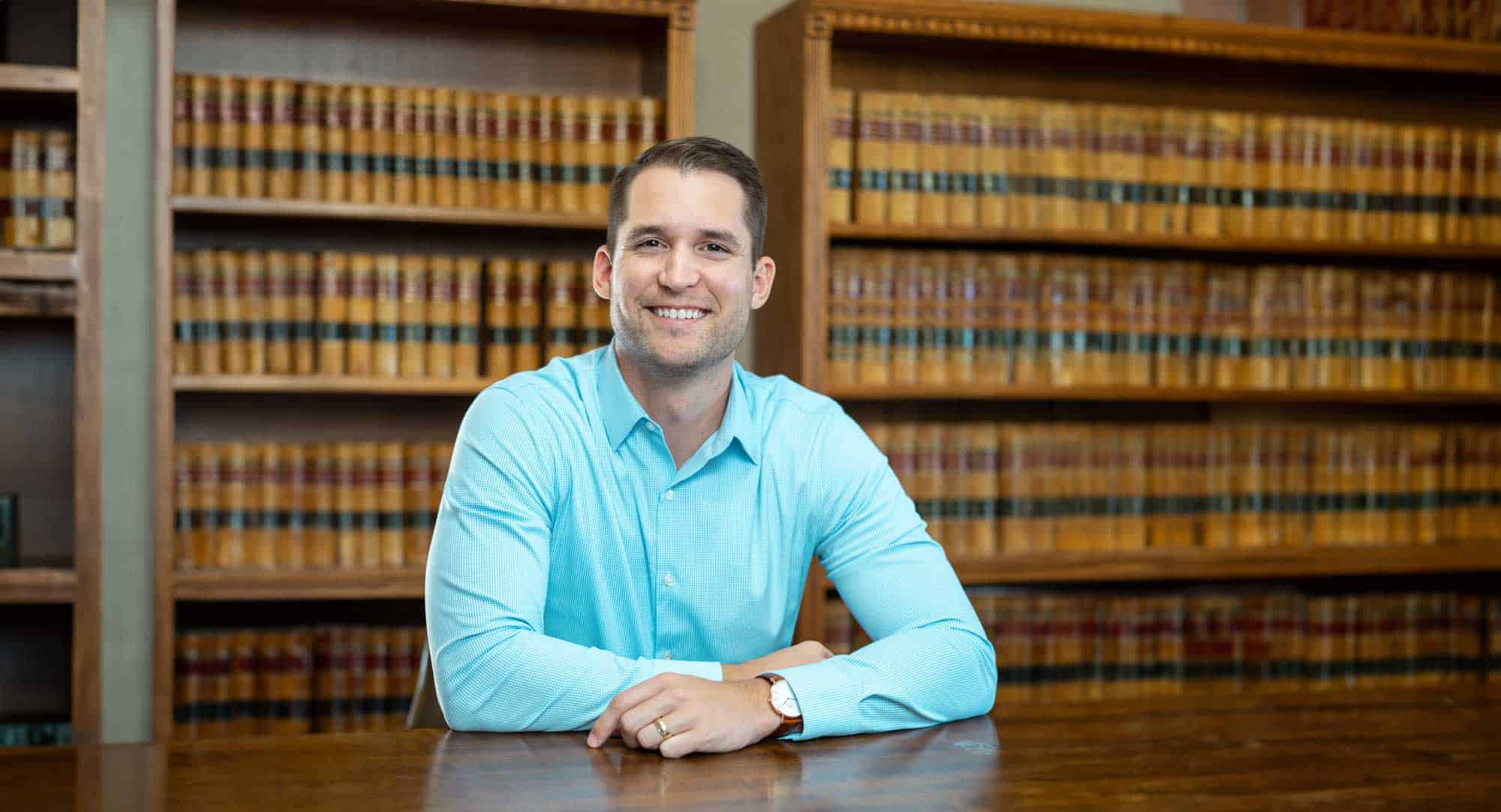 Fisher Firm | A lawyer sitting at a desk in front of a bookcase at a law firm.